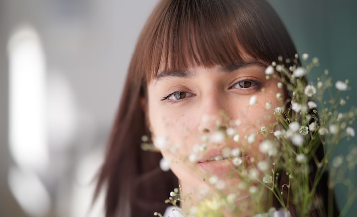 Una fotografía de retrato de una mujer con flequillo y cabello suelto, que mira directamente a la cámara, con un hermoso efecto bokeh creado por la presencia de flores de velo de novia delante de su rostro.